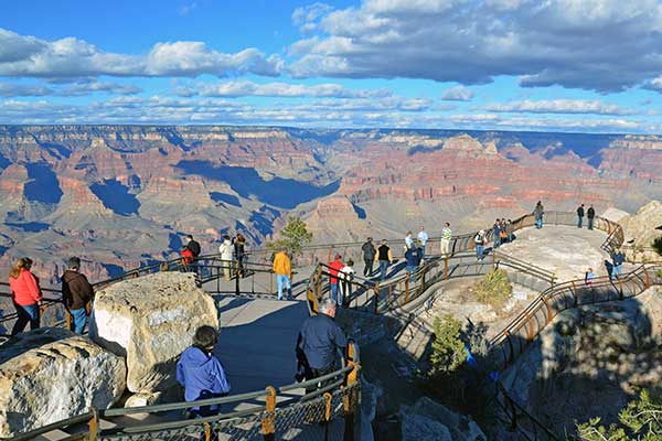 Tourist spread out along the Mather Point Overlook with a beautiful view of the Grand Canyon South Rim on a bright sunny day.
