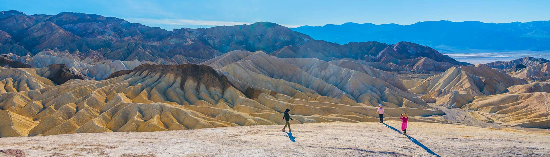 Breathtaking view of Zabrinski Point and the Badlands, with the salt pans of Death Valley in the distance, and three tiny figures in the foreground.