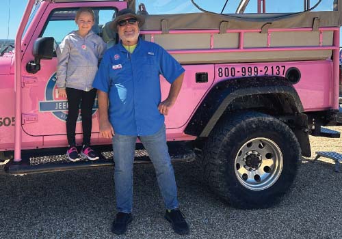 A Pink Jeep Tours adventure guide poses in front of a Pink Jeep with a young girl.