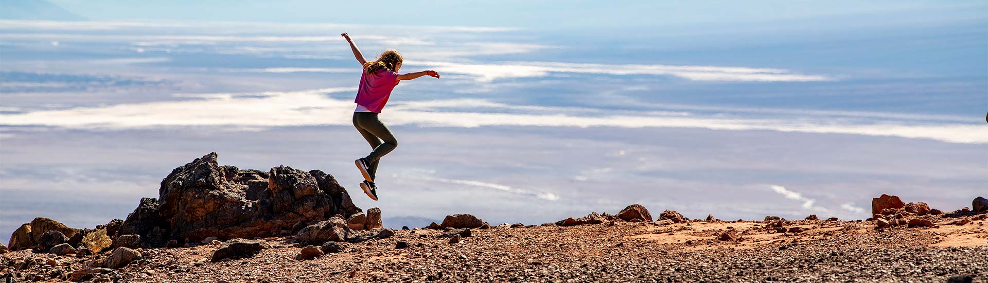Teen girl leaping into the air at edge of Dante's Viewpoint, overlooking the salt pans of Death Valley during Pink jeep Tours Las Vegas tour.