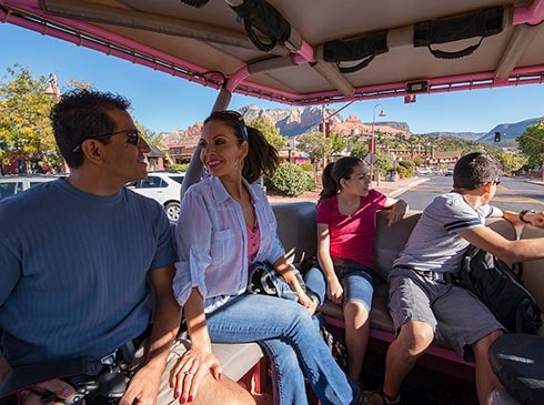 Family of four seated in the back of an open-air Pink Jeep Wrangler riding through Uptown Sedona on the Scenic Sedona Chapel Bells tour.