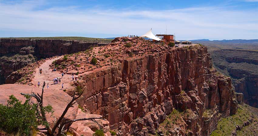 Aerial view of people walking towards the Hualapia Tribe's concessions tents atop Guano Point, with the sheer face of the rock cliff in the foreground.