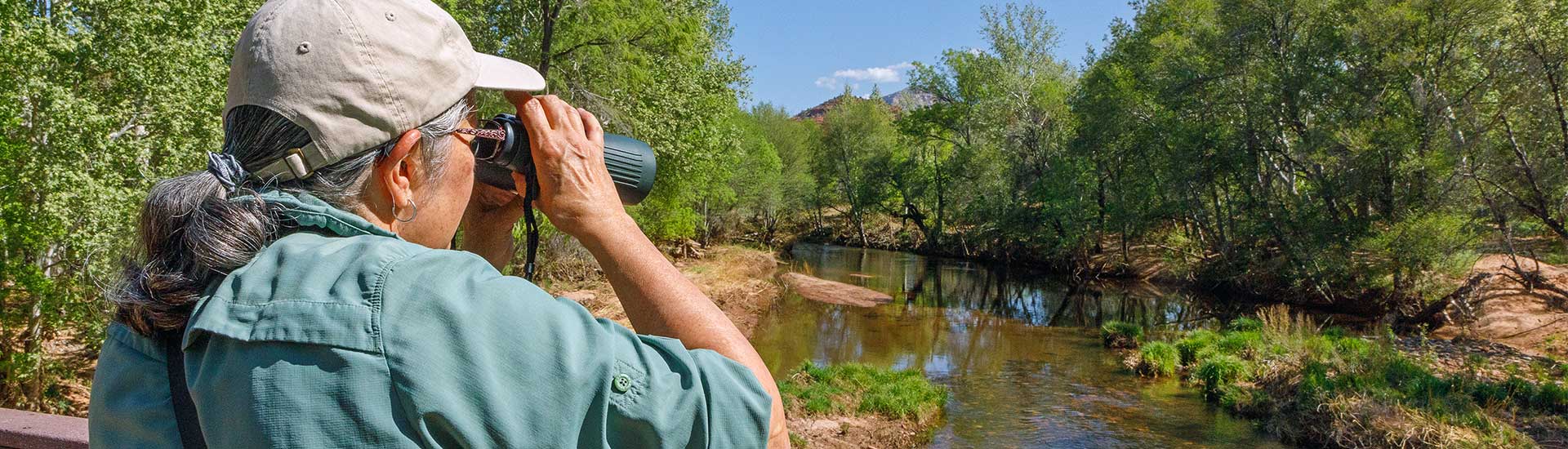 Closeup of a woman looking through binoculars while standing on a bridge over Oak Creek at Red Rock State Park, Sedona, AZ.