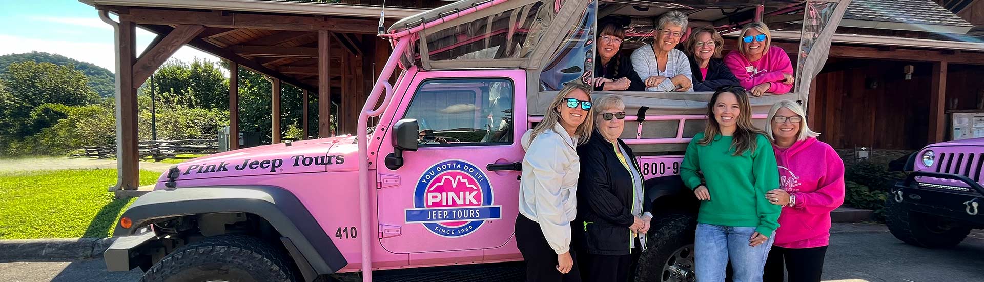 Eight ladies, two with bright pink jackets, posing on a Pink Jeep Wrangler at the Baird Mountain cabin, Pink Jeep Tours Branson.