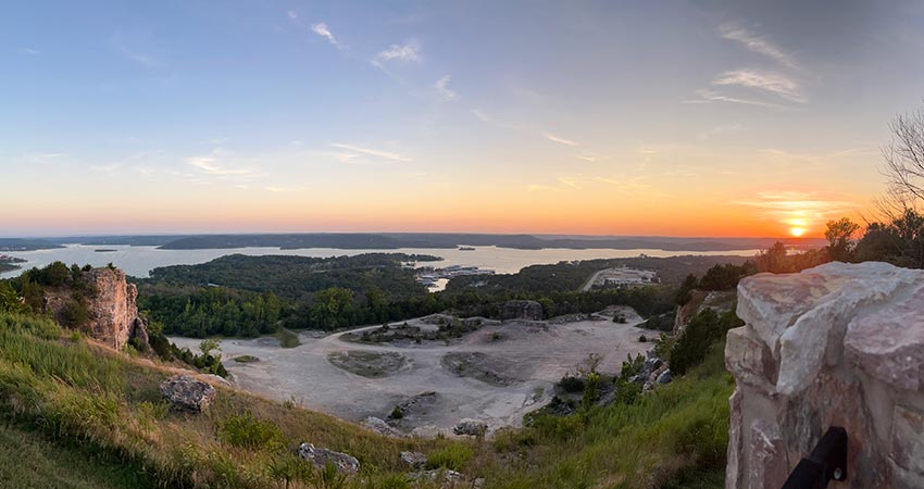View of the rock quarry course below Branson's Baird Mountain with a golden sun dipping below Table Rock Lake, overcast in blue twilight.