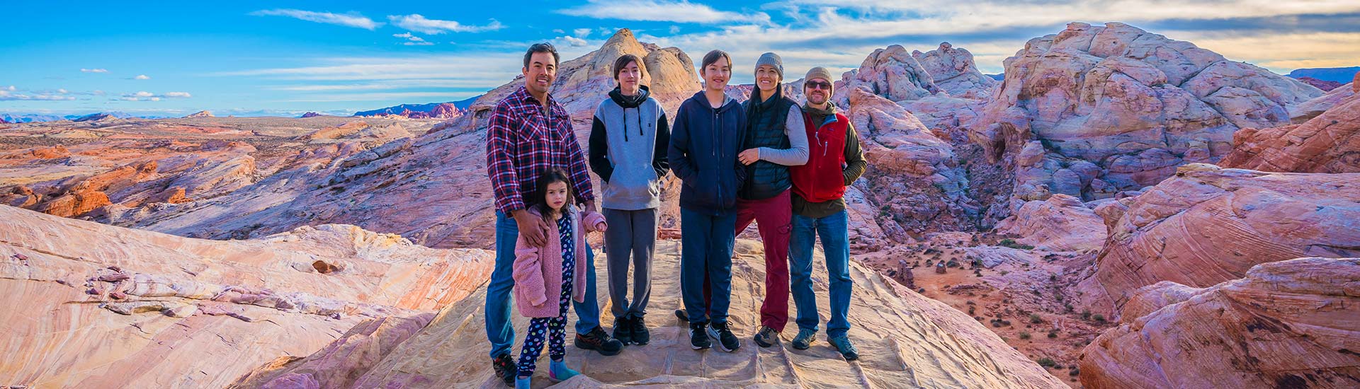 Family with a young girl standing among the rainbow colored rock formations at Valley of Fire State Park with bright blue sky above.