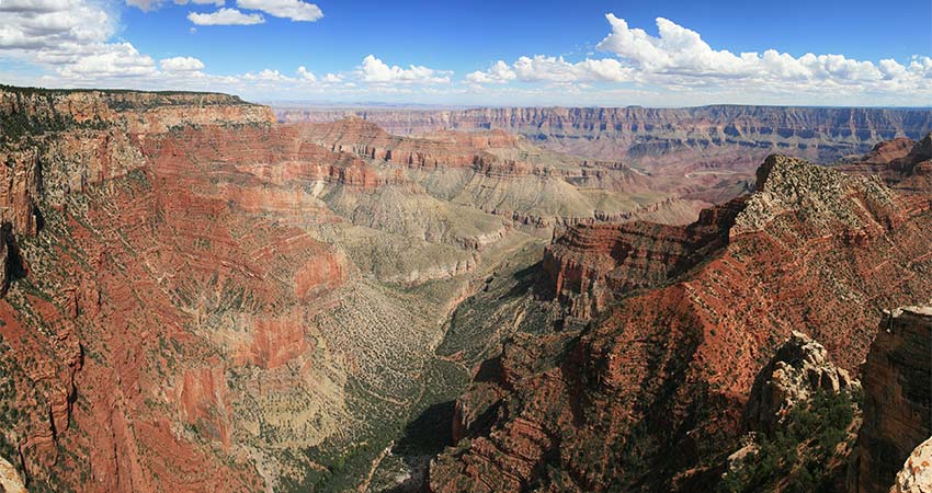 Beautiful aerial view of the multihued rust cliff walls along the Grand Canyon West Rim with a narrow green valley below and blue sky above.
