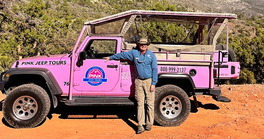 Pink Jeep Tours Las Vegas adventure guide stands next to a vibrant pink Jeep Wrangler parked along the Rocky Gap Road in Red Rock Canyon, Nevada.