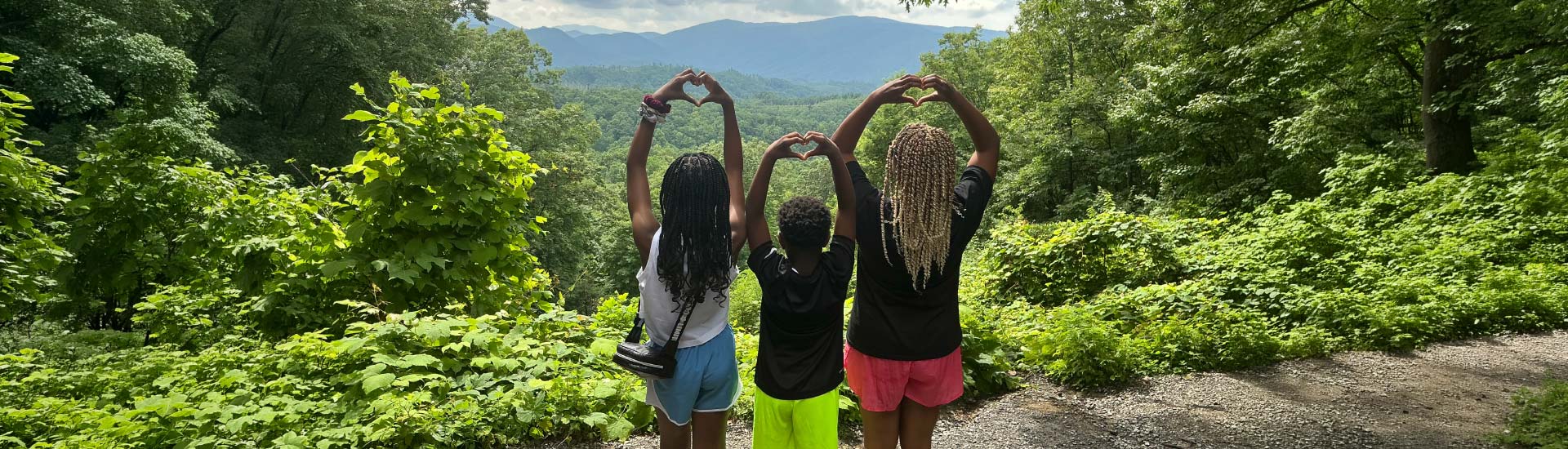 Three children stand looking out across the Smokies, forming hearts with their hands above their heads