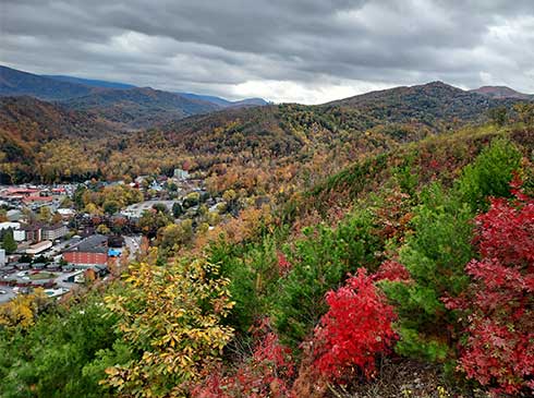Aerial view of Downtown Gatlinburg and surrounding hills with vibrant red, green and gold fall foliage in the foreground.