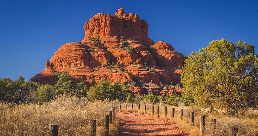 Red dirt pathway leading to Bell Rock Vista in Sedona, Arizona surrounded by desert foliage and trees, Pink Jeep Scenic Sedona tour.