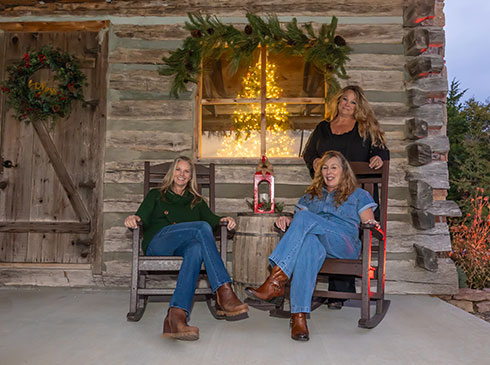 Three women seated on the porch of the Branson Christmas Cabin atop Baird Mountain, Pink Jeep Tours Branson, MO.