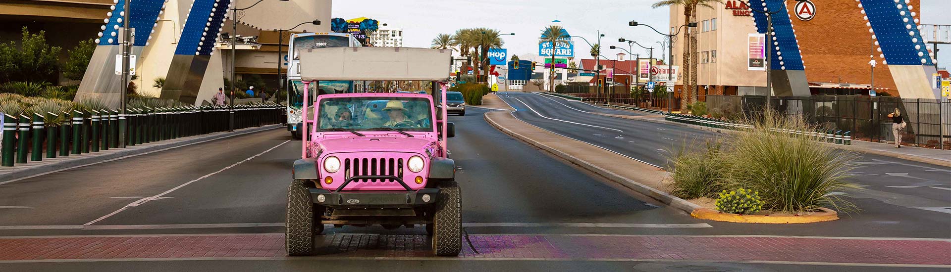 Pink Jeep Wrangler driving towards the camera along Las Vegas Boulevard during day time, Pink Jeep Tours Vintage Vegas Tour.