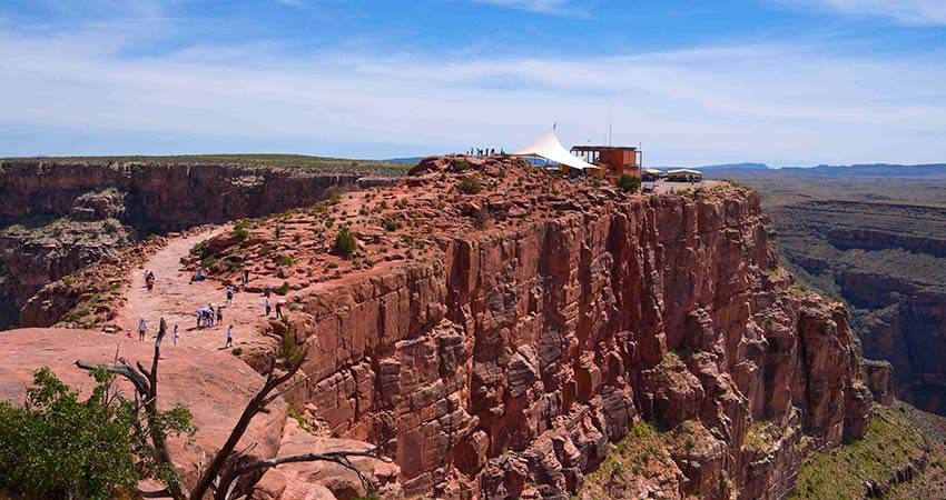 Aerial view of people walking towards the Hualapia Tribe's concessions tents atop Guano Point, with the sheer face of the rock cliff in the foreground.