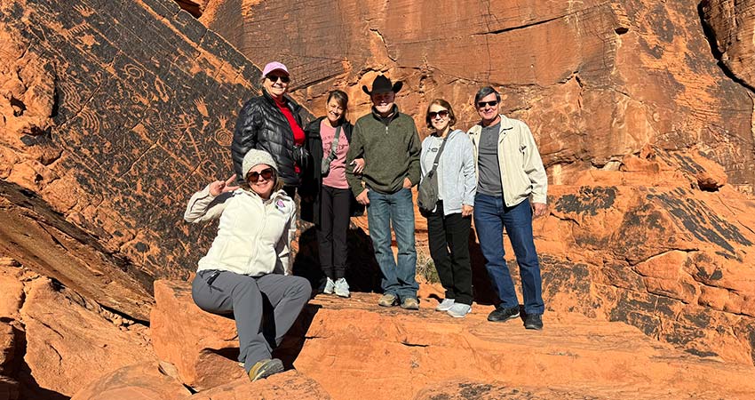Three couples posing next to a petroglyph wall at Valley of Fire State Park on Pink Jeep Tours Hoover Dam Valley of Fire Tour, from Las Vegas.