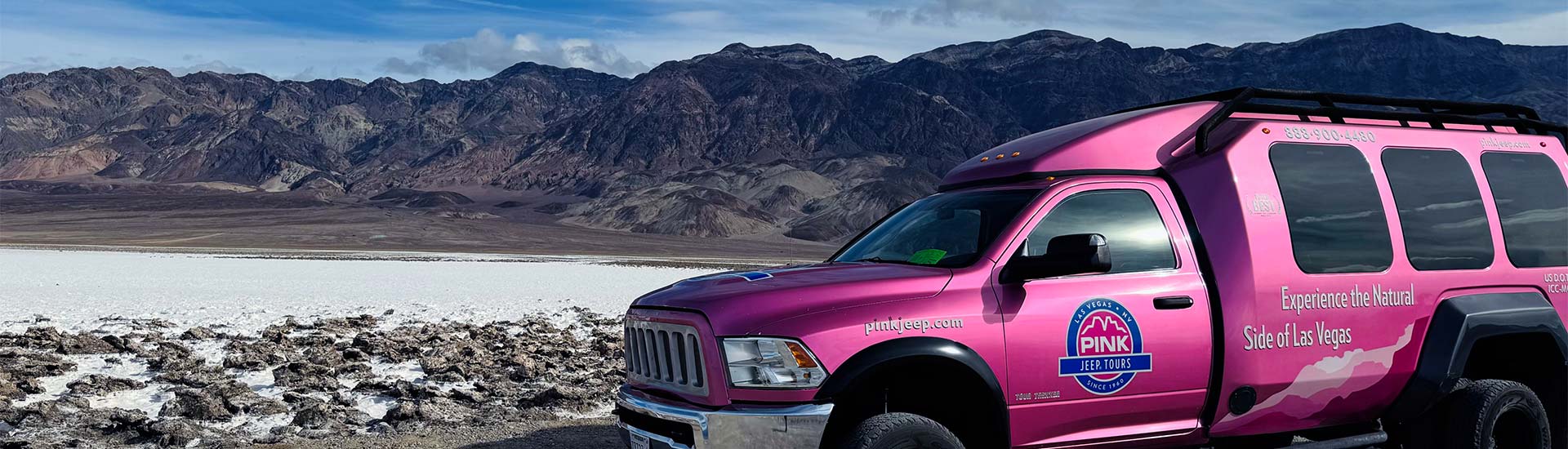 Pink Adventure Tour Trekker parked alongside the salt flats at Death Valley National Parks with dramatic mountains in the background.
