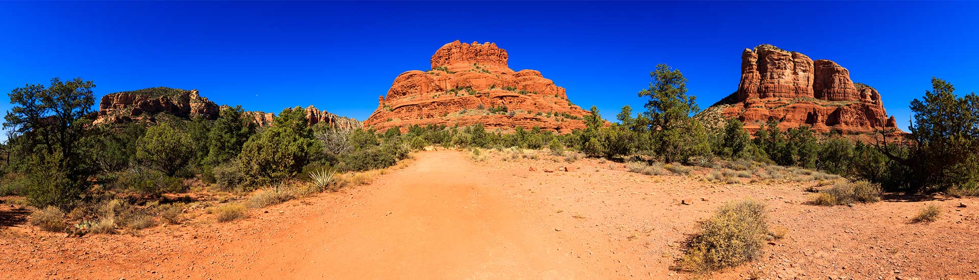 Panoramic view of Bell Rock and Courthouse Butte in Sedona, Arizona against a brilliant deep blue sky.