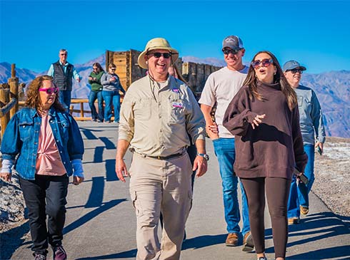 Pink Jeep Tours Las Vegas adventure guide and guests touring Harmony Borax Works with the Twenty Mule Team Wagon replica in the background.