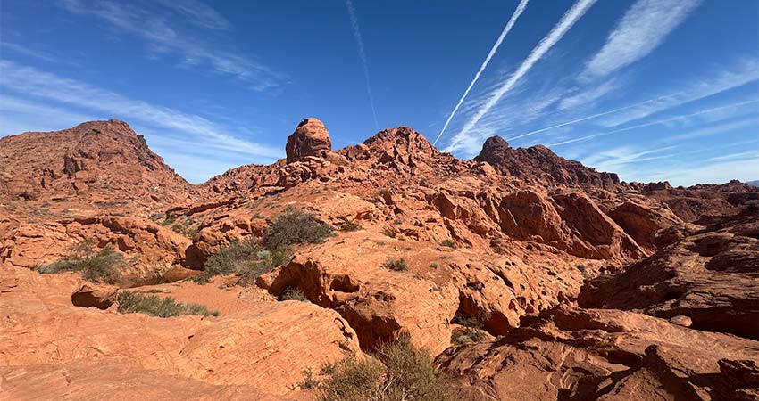 Aztec sandstone formations and rocky landscape at Valley of Fire State Park with contrails shooting across a clear blue sky towards the camera.