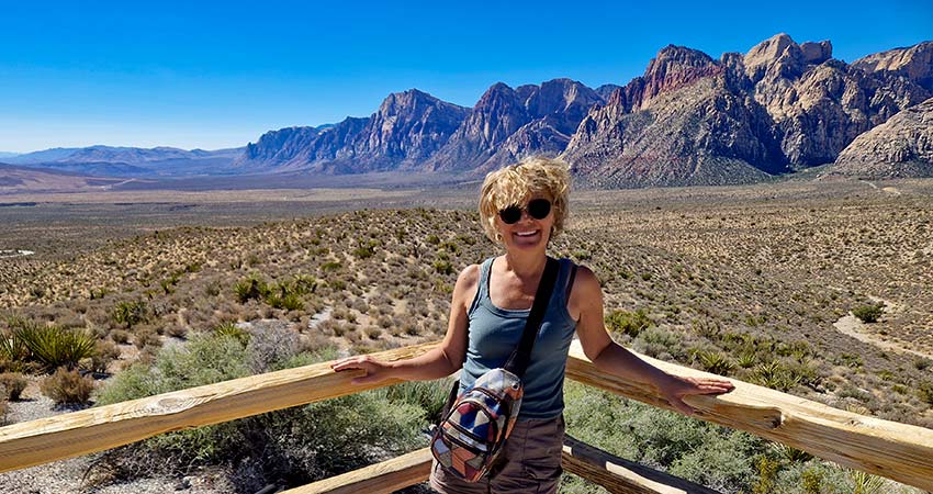 Woman smiling and posing at a popular viewpoint at Red Rock Canyon with grasslands and rock formations in the background.