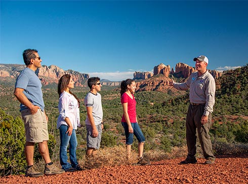 Pink Jeep tour guide and guests at The Knolls viewpoint with panoramas of Cathedral Rock landscape in the distance.