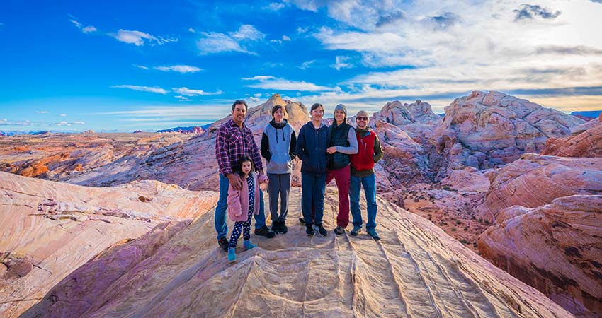 A large family with a young girl standing among rainbow colored rock formations at Valley of Fire State Park under a vibrant blue sky.