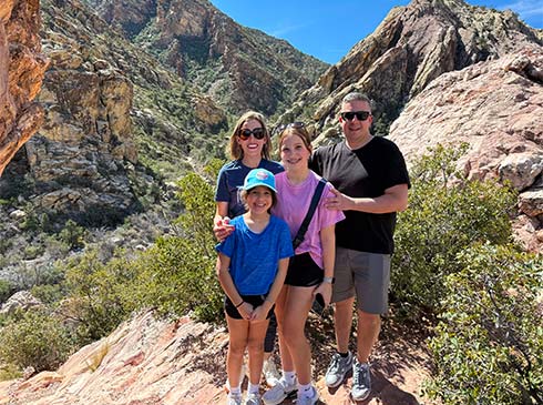 Parents and two kids posing among large boulders and green brush in Red Rock Canyon on the Pink Jeep Red Rock Canyon Tour.