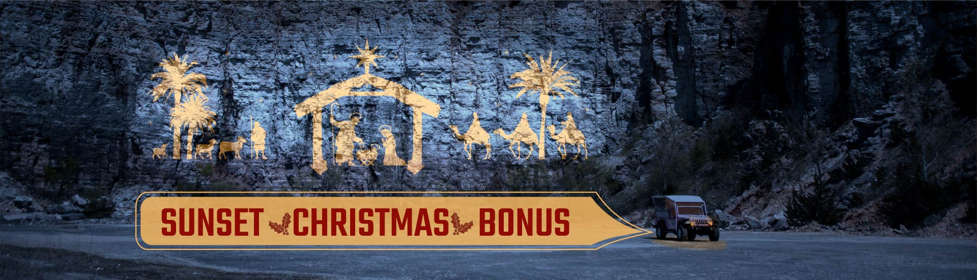 Nighttime view of a  Pink Jeep traveling past a light-projected nativity scene on the cliffside of Baird Mountain, with Sunset Christmas Bonus banner.