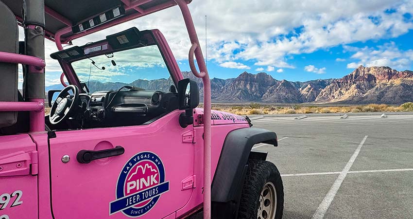 Pink Jeep Tours' Jeep Wrangler parked facing a mountain range at Red Rock Canyon National Conservation Area, with windshield view of landscape.