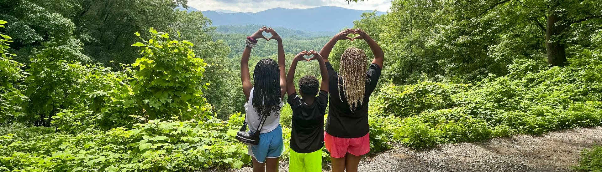 Three children stand looking out across the Smokies, forming hearts with their hands above their heads