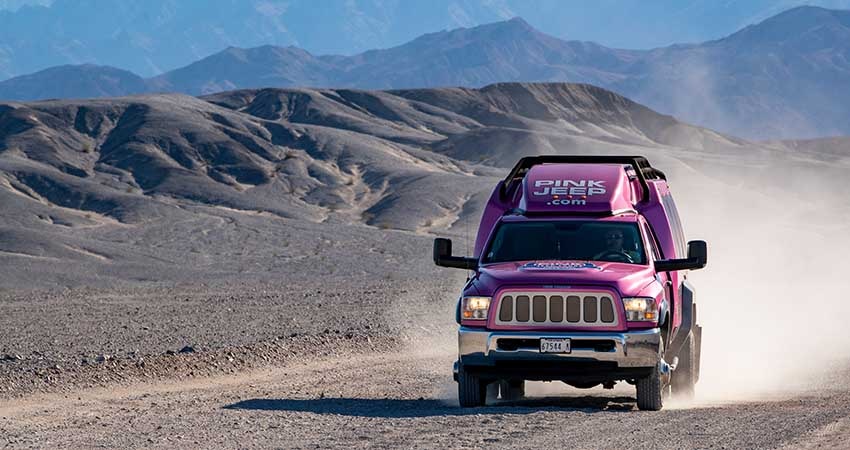 Pink Jeep Las Vegas tour trekker driving towards the camera on a dirt road flanked by the hills of Death Valley National Park.