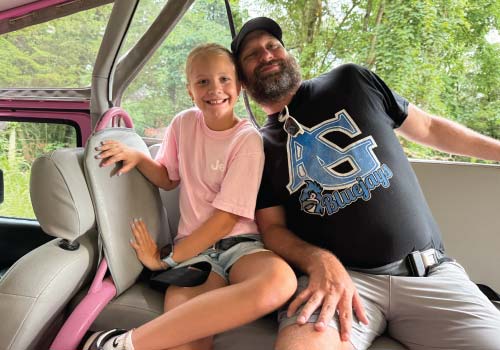 A father and his young daughter playfully pose in the back of a Pink Jeep while on tour.