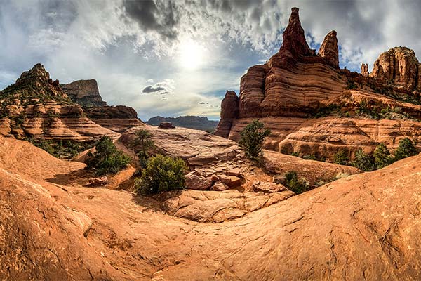 Panoramic view of Sedona's Chicken Point along the Broken Arrow Trail, where layered red rock formations rise beneath dramatic clouds and bright desert sun.