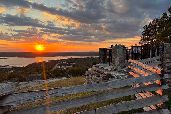 Visitors watch an orange sunset over Table Rock Lake from Pink Jeep Tours' exclusive Baird Mountain overlook, as the sun casts sparkling rays across the water.