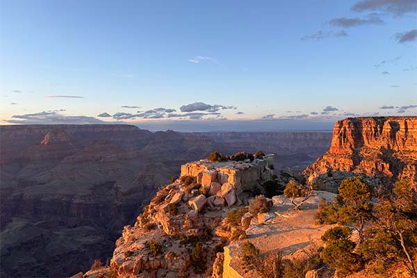 View of the Grand Canyon during the golden hour as sunlight casts a warm, rose-colored hue over rocky cliffs in the foreground.