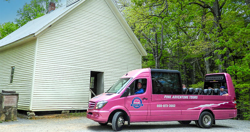 Smoky Mountain Pink Jeep Tours PanoramaVan is parked in front of a white historic church on the Cades Cove Tour.