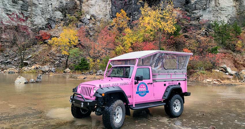 Pink Jeep Wrangler at the bottom Baird Mountain rock quarry, with vibrant fall foliage in the background, Pink Jeep Tours Branson.