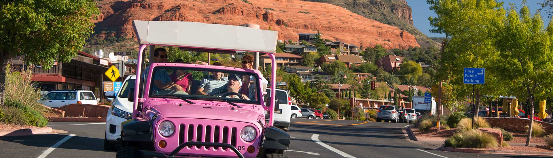 Pink Jeep Wrangler driving towards camera in Uptown Sedona with guests on the Scenic Sedona tour.