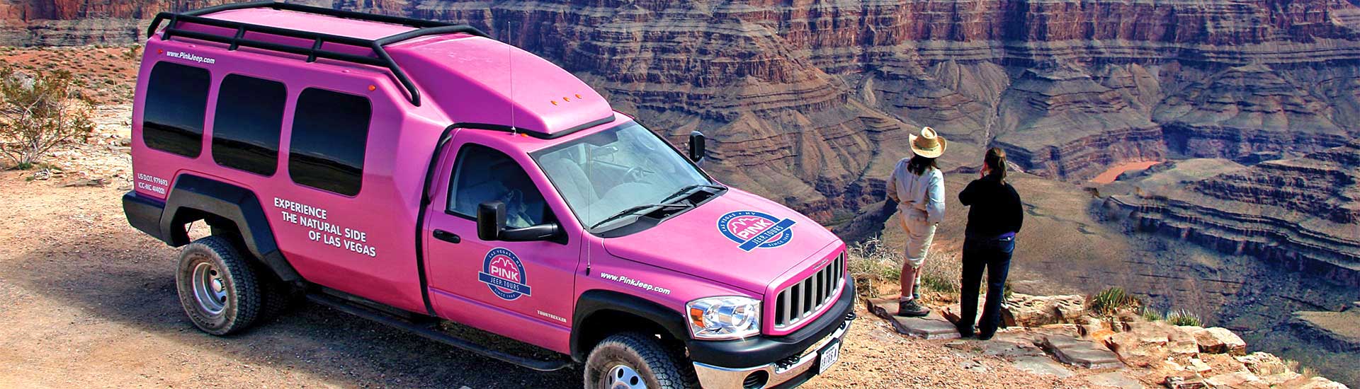 Two people standing outside a Las Vegas Pink Jeep Tours' adventure trekker peering over the edge of the Grand Canyon West Rim.