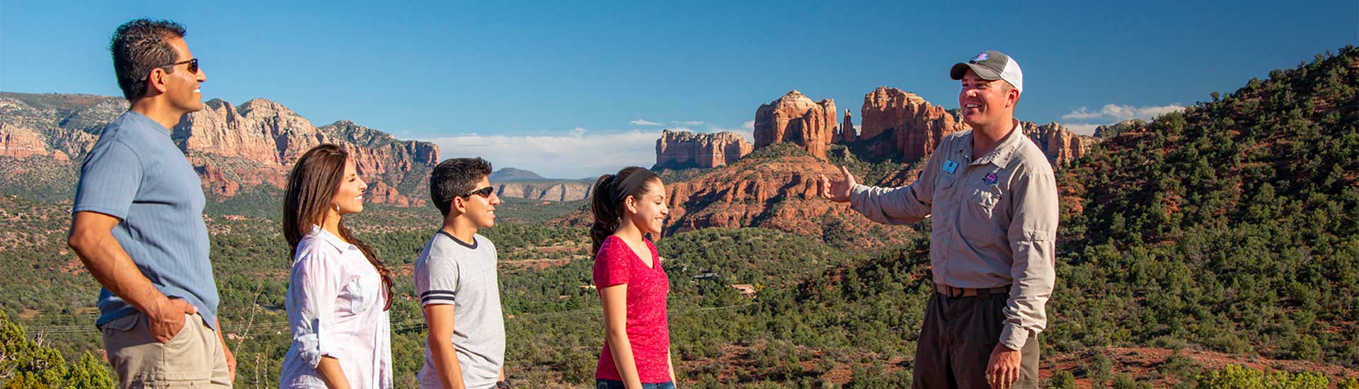 Pink Jeep Sedona tour guide talking with a family at a viewpoint overlooking the Cathedral Rock landscape from Upper Red Rock Loop Road, Sedona, AZ.
