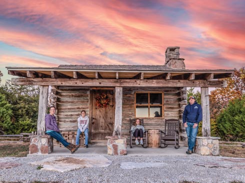 A family sits on the porch of a festival log cabin in Branson, MO.