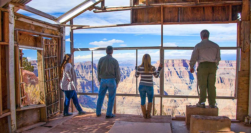 Four people standing in a building looking out floor-to-ceiling windows overlooking the Grand Canyon West Rim, Pink Jeep Tours.