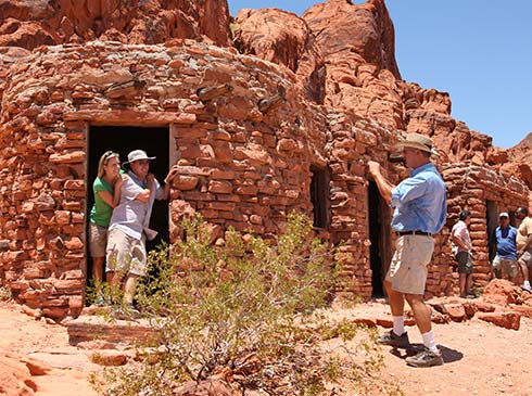 Pink Jeep Las Vegas tour guide taking a photo of a couple standing in the entryway of a stone Cabin at Valley of Fire State Park. 