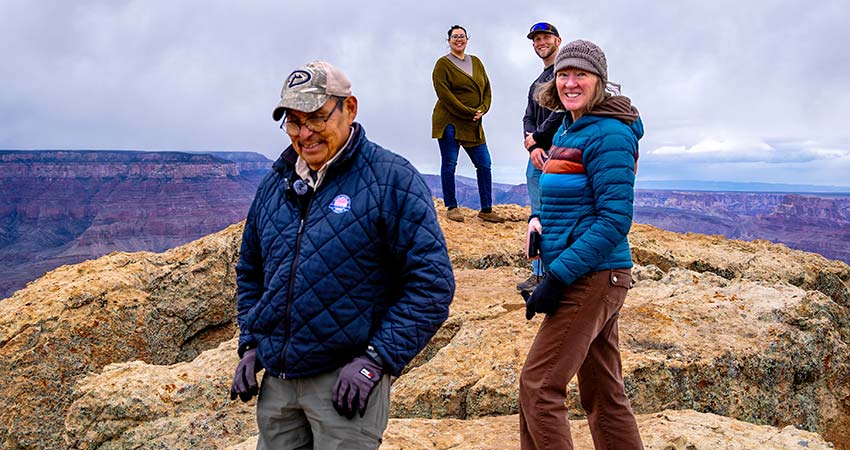 Pink Jeep Tours Grand Canyon adventure guide with three guests smiling while walking atop a rocky ledge overlooking the Grand Canyon.