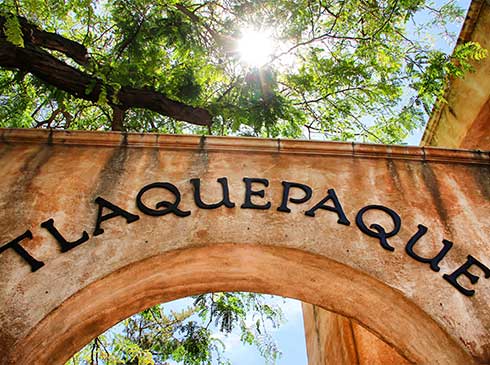 Sun starburst beaming over the archway of Tlaquepaque Arts and Crafts Village surrounded by sycamore trees, Sedona, Arizona.