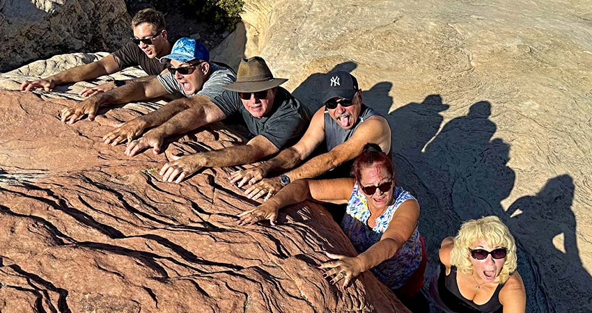Fun group of six adults appearing to hang off a rock ledge at Red Rock Canyon during Pink Jeep Tours Las Vegas to Red Rock Canyon tour.