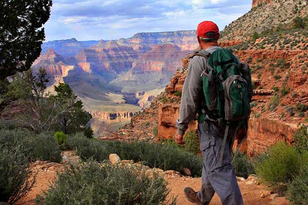 A man with a backpack walks along the Rim Trail overlooking the Grand Canyon South Rim at Grand Canyon National Park.