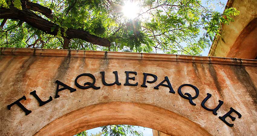Tlaquepaque Arts and Crafts Village archway sign with sunburst beaming through the sycamore trees above it, Sedona, Arizona.