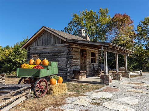 Historic log cabin on Baird Mountain with a pumpkin wagon parked nearby and fall foliage in Branson, Missouri.