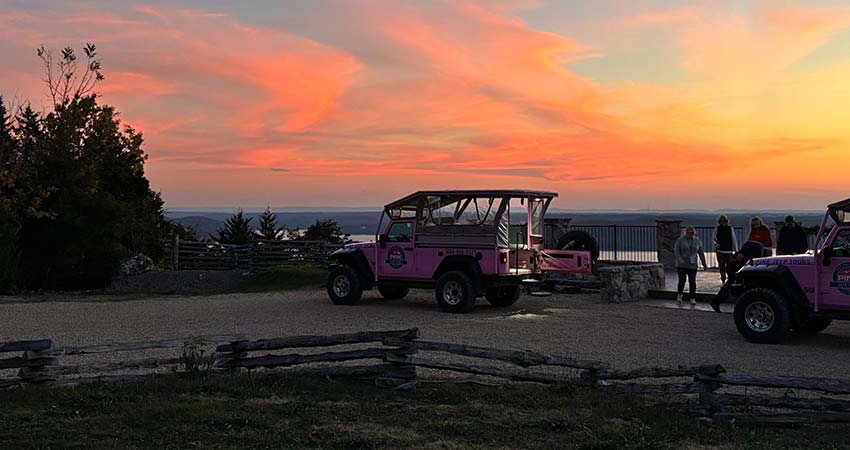 Two Pink Jeep Wrangler's parked atop the Baird Mountain Table Rock Lake overlook at dusk, with a vibrant pink and orange sunset above.